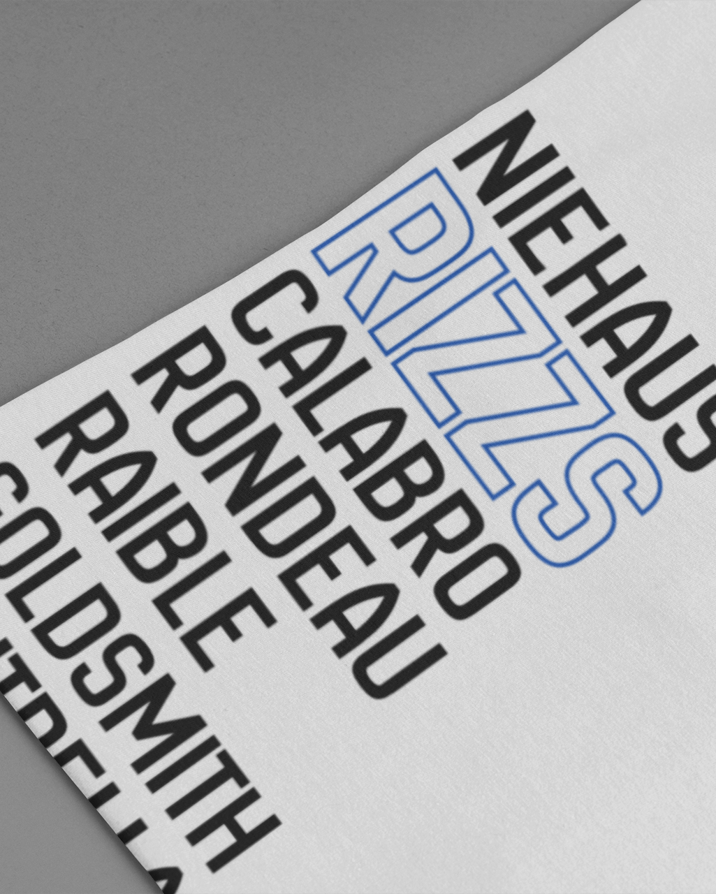 A close-up of a white t-shirt laid flat on a gray background, featuring a graphic print of golf course names in black and blue text.