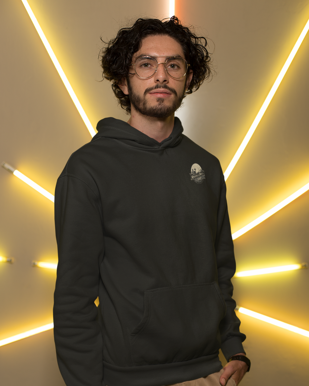 Man wearing a black hoodie with a logo against a wall with neon lighting