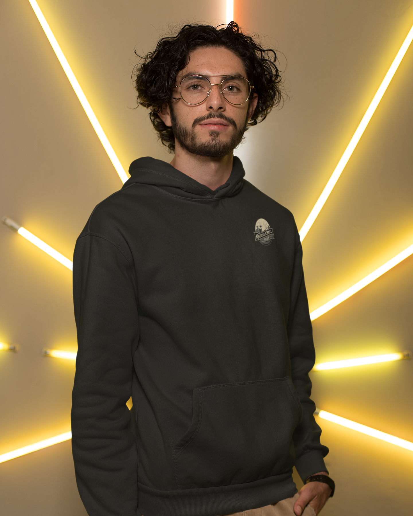 Man wearing a black hoodie with a logo against a wall with neon lighting