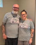A man and a woman standing indoors wearing matching gray t-shirts with 'SPOKANE STRONG' Roots Run Deep printed on the front.