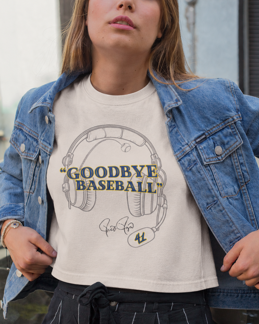Model in an ivory boxy tee with a headset graphic and blue-and-yellow “Goodbye Baseball” lettering under a denim jacket.