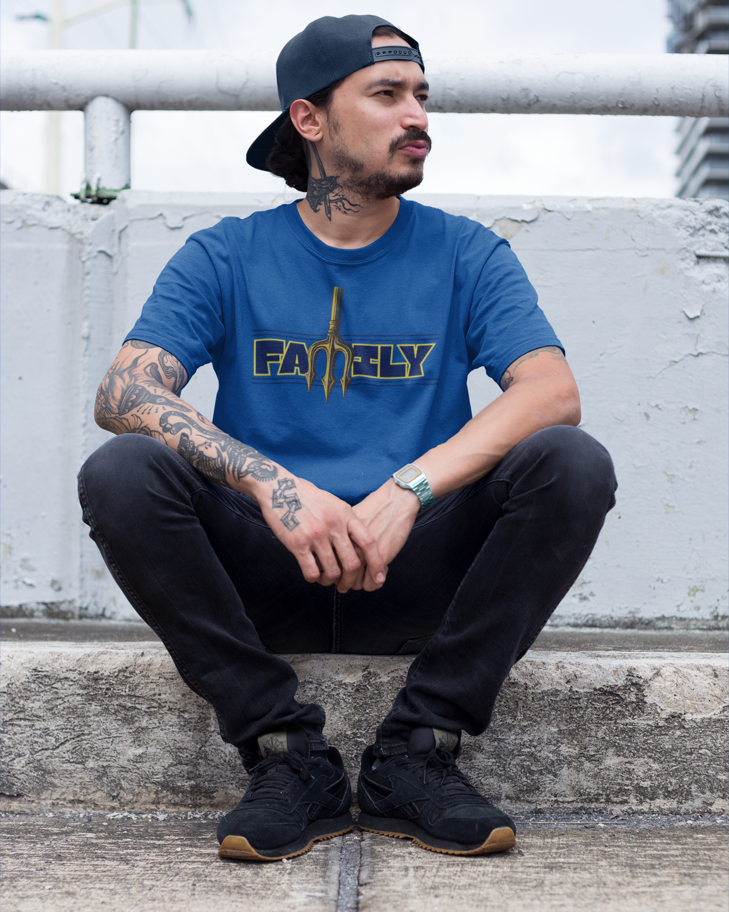 Man wearing a blue t-shirt with 'FAMILY' logo sitting on concrete sidewalk.