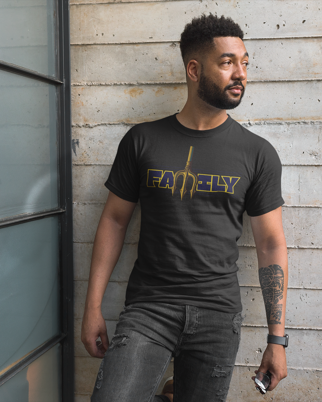 Man wearing a black t-shirt with 'FAMILY' printed on it, standing against a wooden wall.