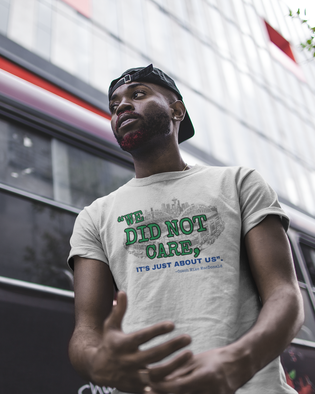 Man wearing a grey t-shirt with design that says "We Did Not Care" in front of a bus