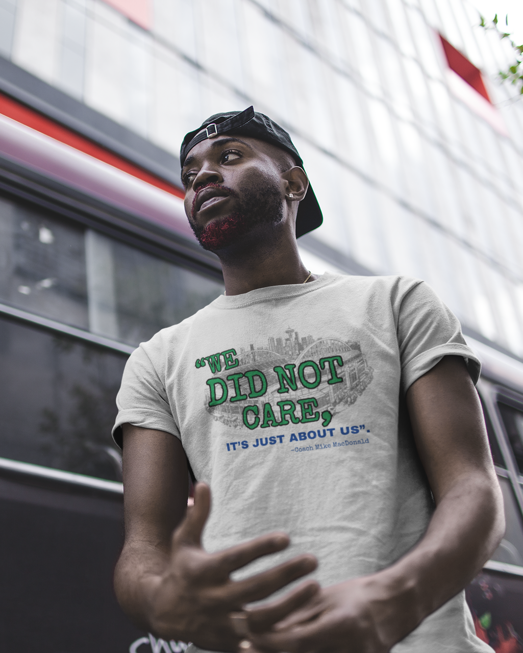 Man wearing a grey t-shirt with design that says "We Did Not Care" in front of a bus