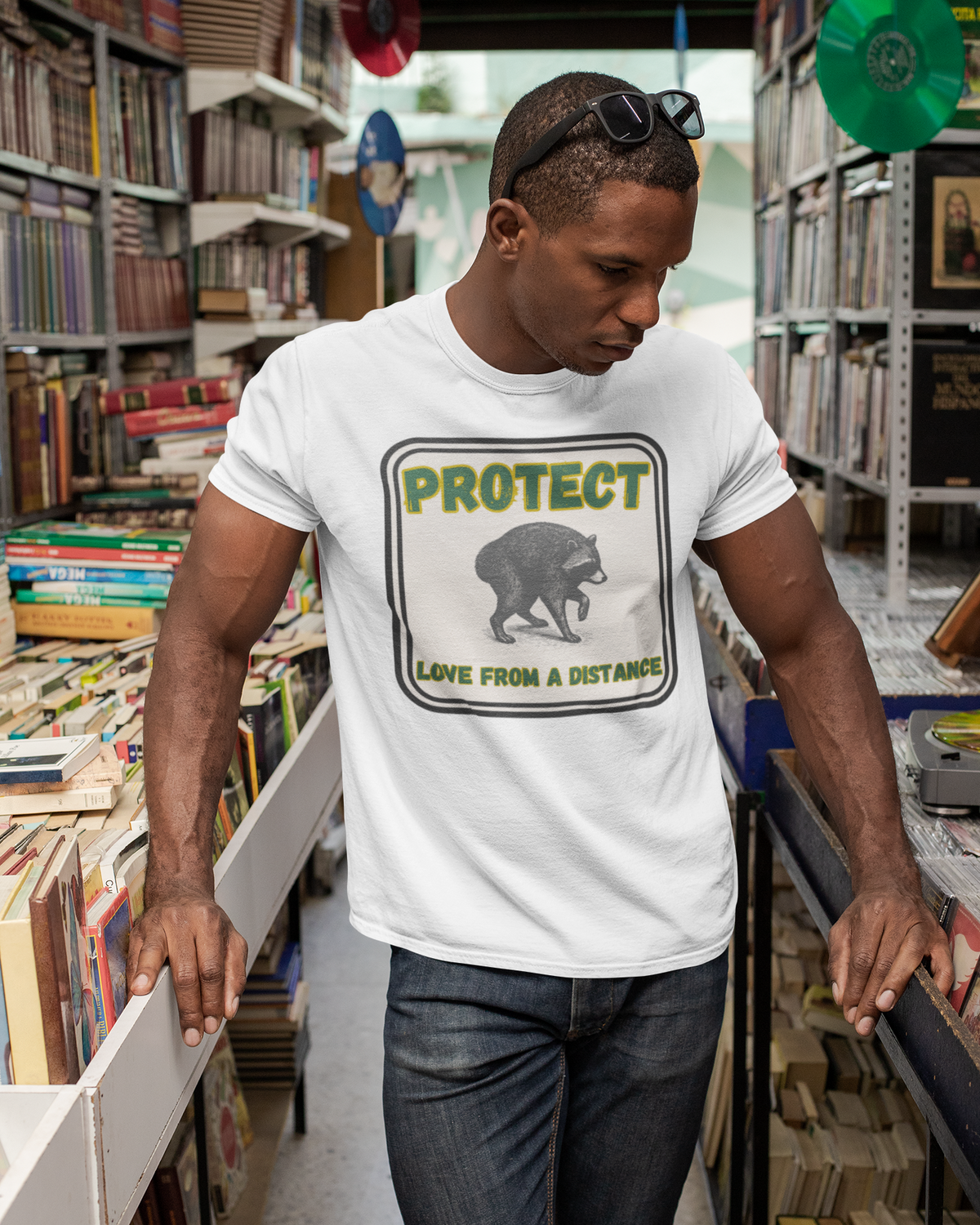 A man wearing a white graphic t-shirt with a bear design and the text 'PROTECT LAKE FROM A DISTANCE' walks down an aisle in a bookshop.