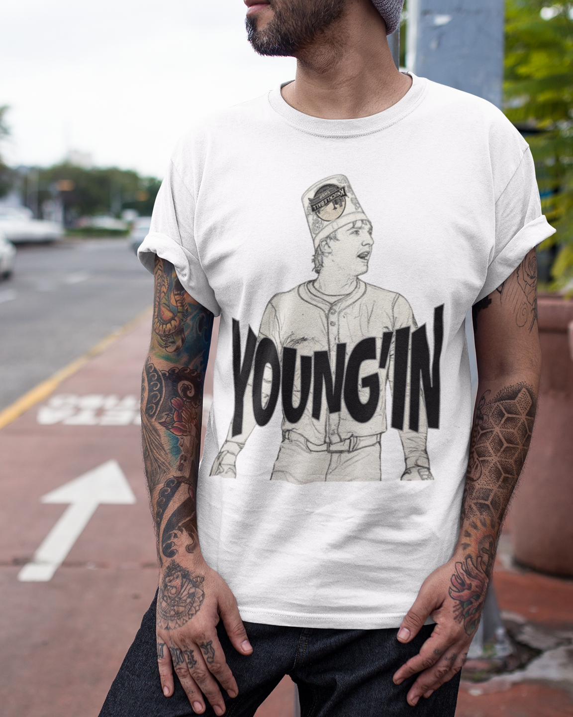 A man wearing a white graphic t-shirt with a black and gray illustration and the text 'YOUNG'IN' printed on the front, standing on a city street.