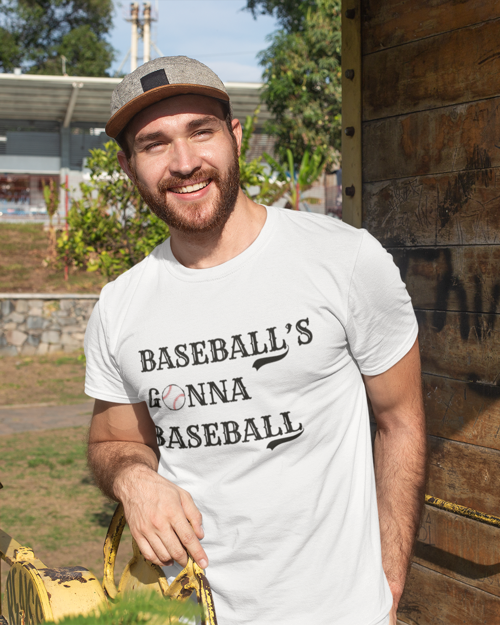 Man wearing a white t-shirt with 'BASEBALL'S GONNA BASEBALL' text, standing outdoors.