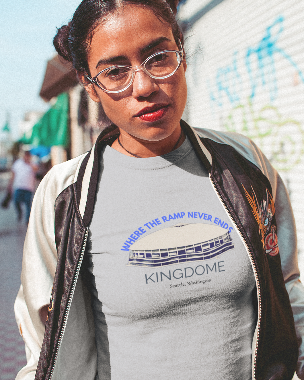 Young lady wearing a t-shirt with 'Kingdome' text and graphics on a city street.