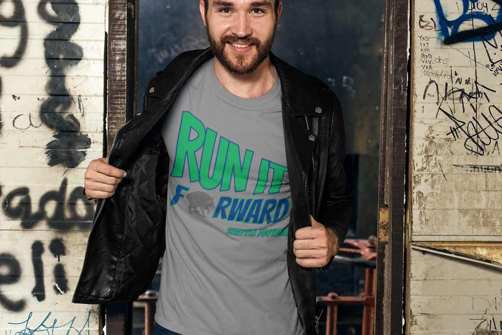 A smiling man wearing a gray t-shirt with a green and blue 'RUN IT FORWARD' graphic, styled with an open black leather jacket, standing in a graffiti-covered doorway.