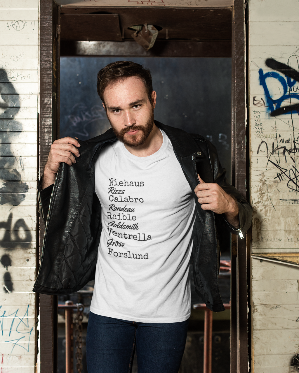 Man wearing a white t-shirt with text, standing in a doorway with graffiti on the wall.